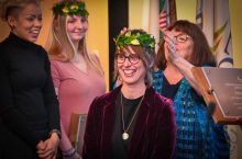 Dr. Jenna Goldsmith, ISU alum, is crowned poet laureate of Rockford, Il. She is wearing a maroon velvet blazer and a crown of leaves.